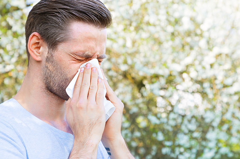 Man blowing his nose because of seasonal allergic rhinitis symptoms